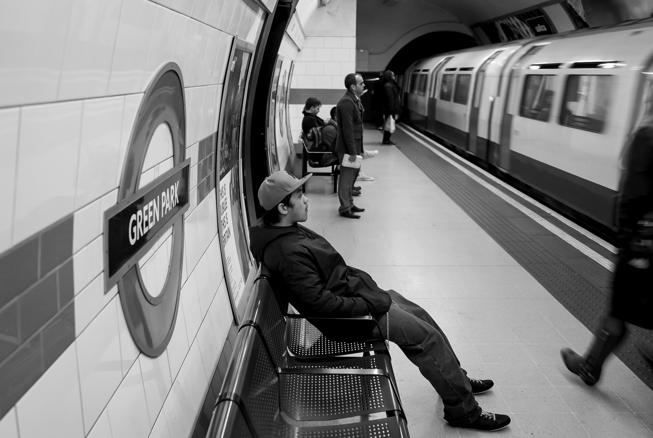 Commuters at Green Park Underground with a boy lying on a bench