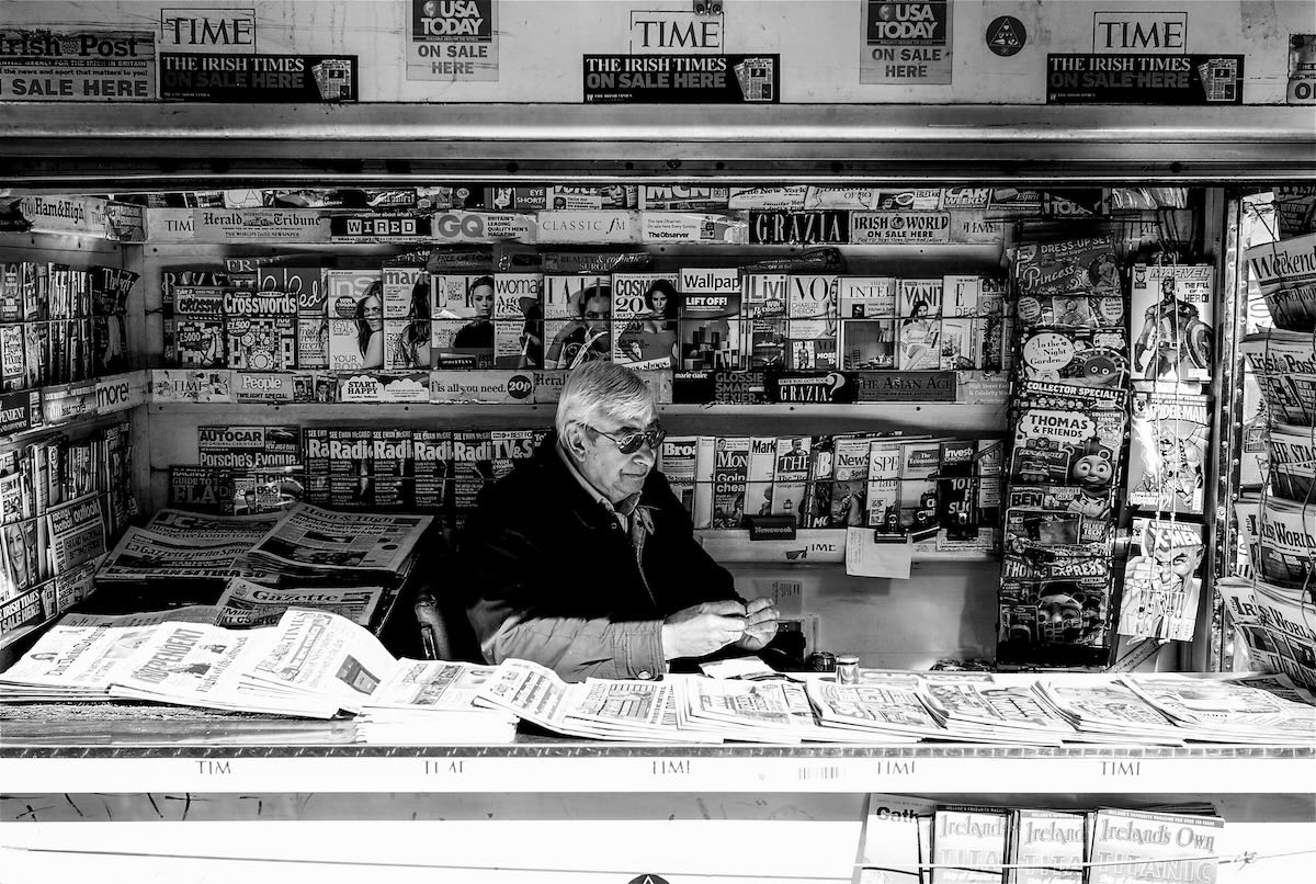 Man selling newspapers and magazines at a London newspaper stand, photographed on a Leica M8