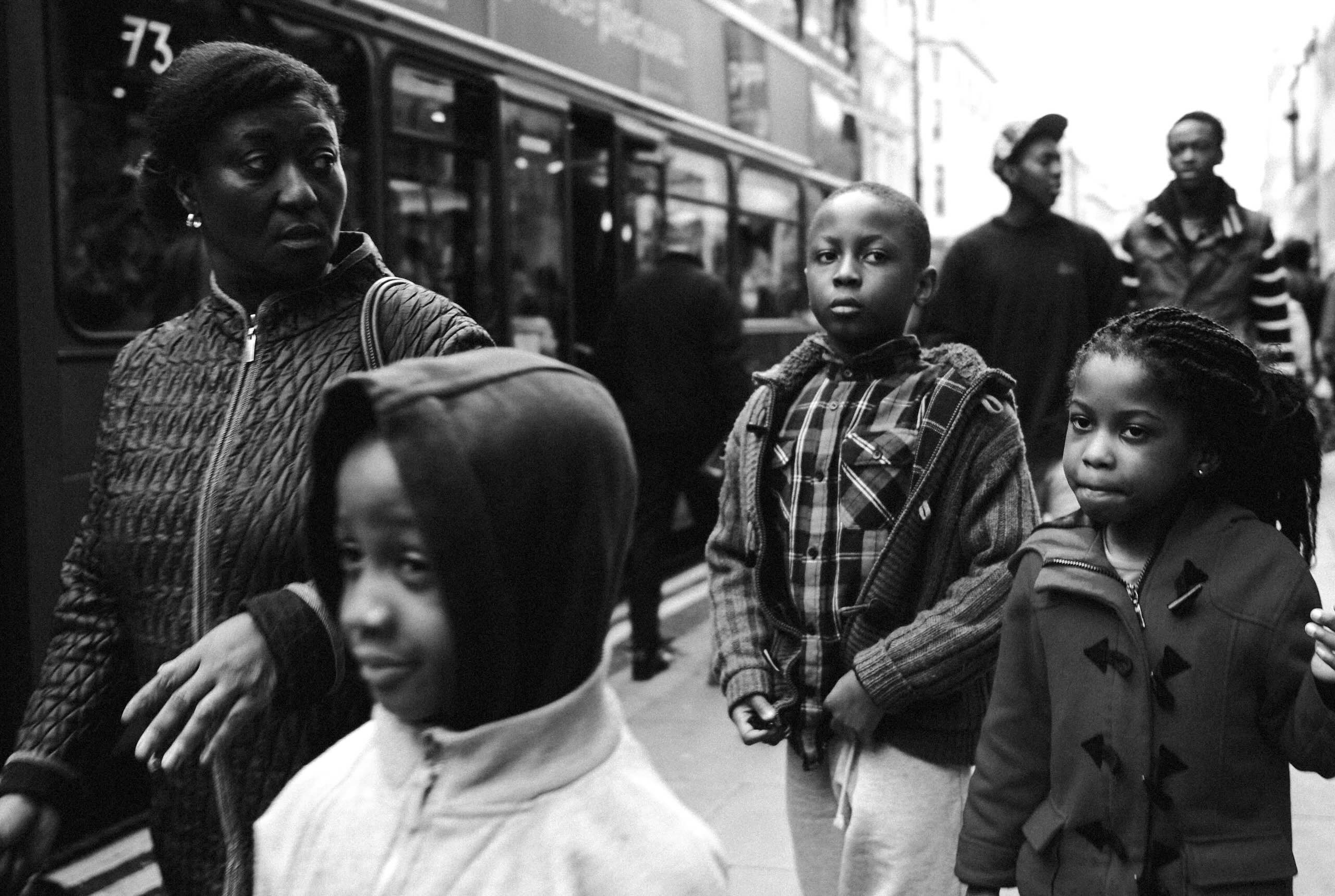 Black and white street photograph of a family walking along Oxford Street in London with a number 73 bus passing by
