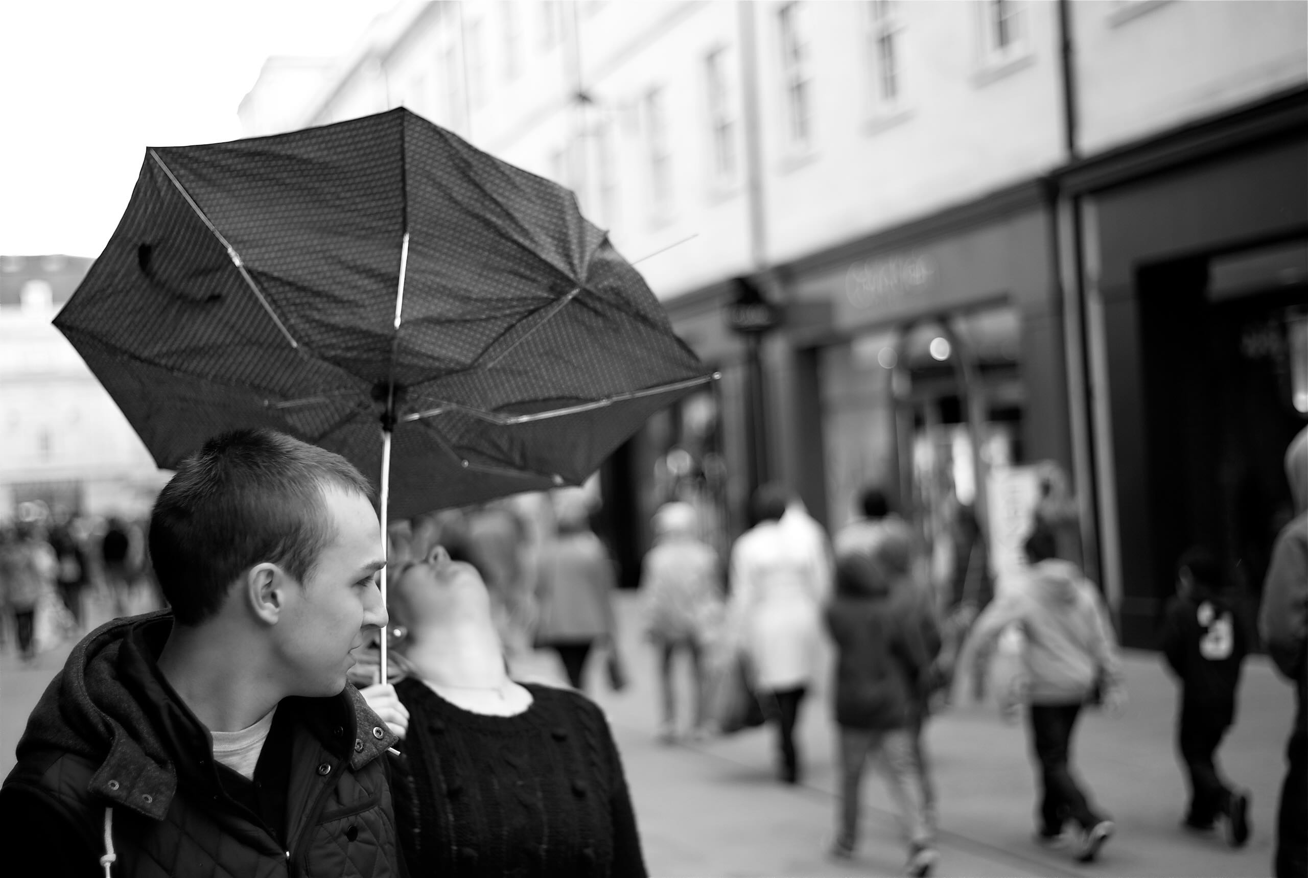 Candid street photograph of a couple walking in London as the wind turns the woman’s umbrella inside out